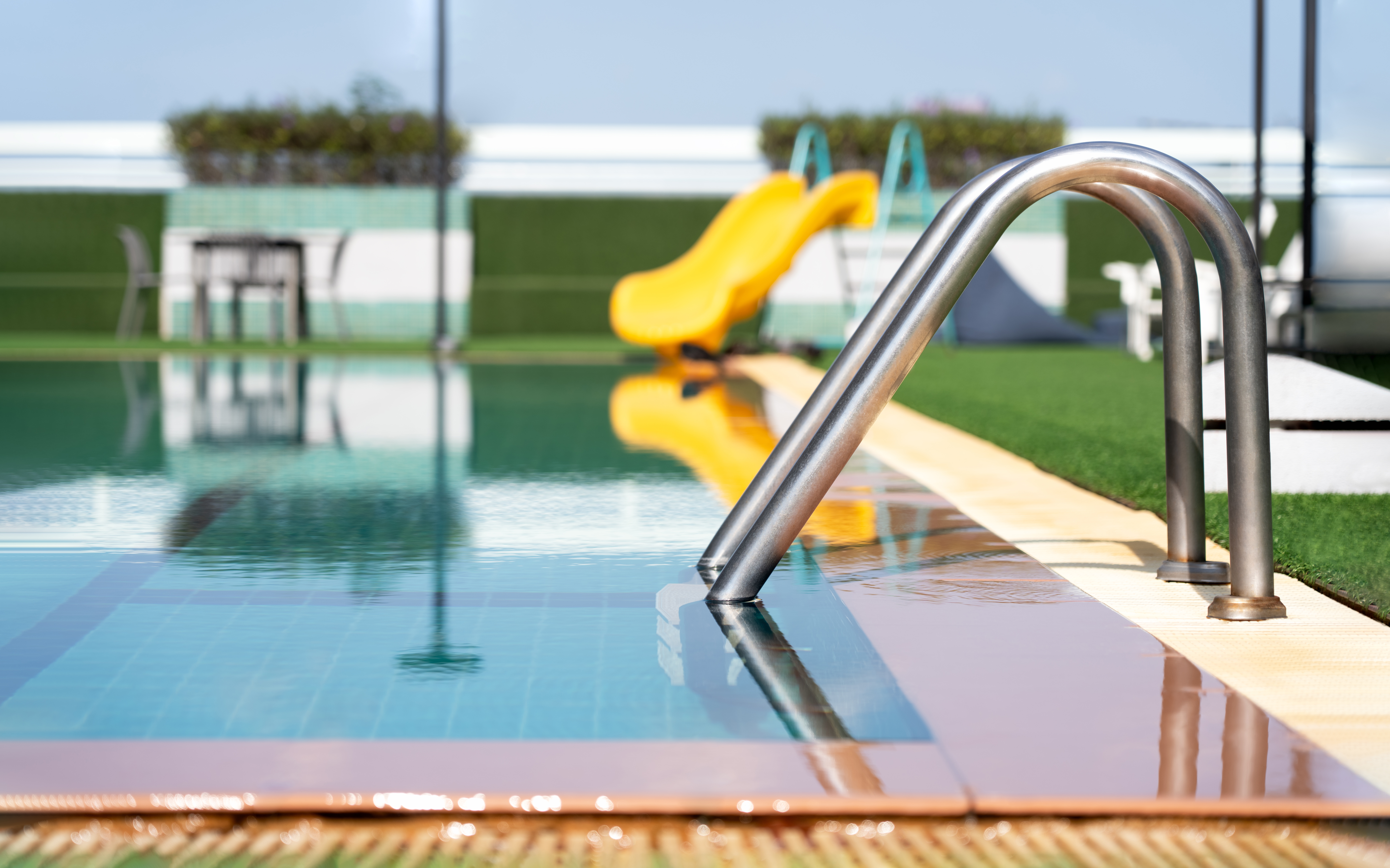 Swimming pool with stair ladder in the clear water.Poolside with Stainless steel handrail in to blue water and ground floor ceramic tiles,Cancept for satying in Hotel on Holiday Vacation