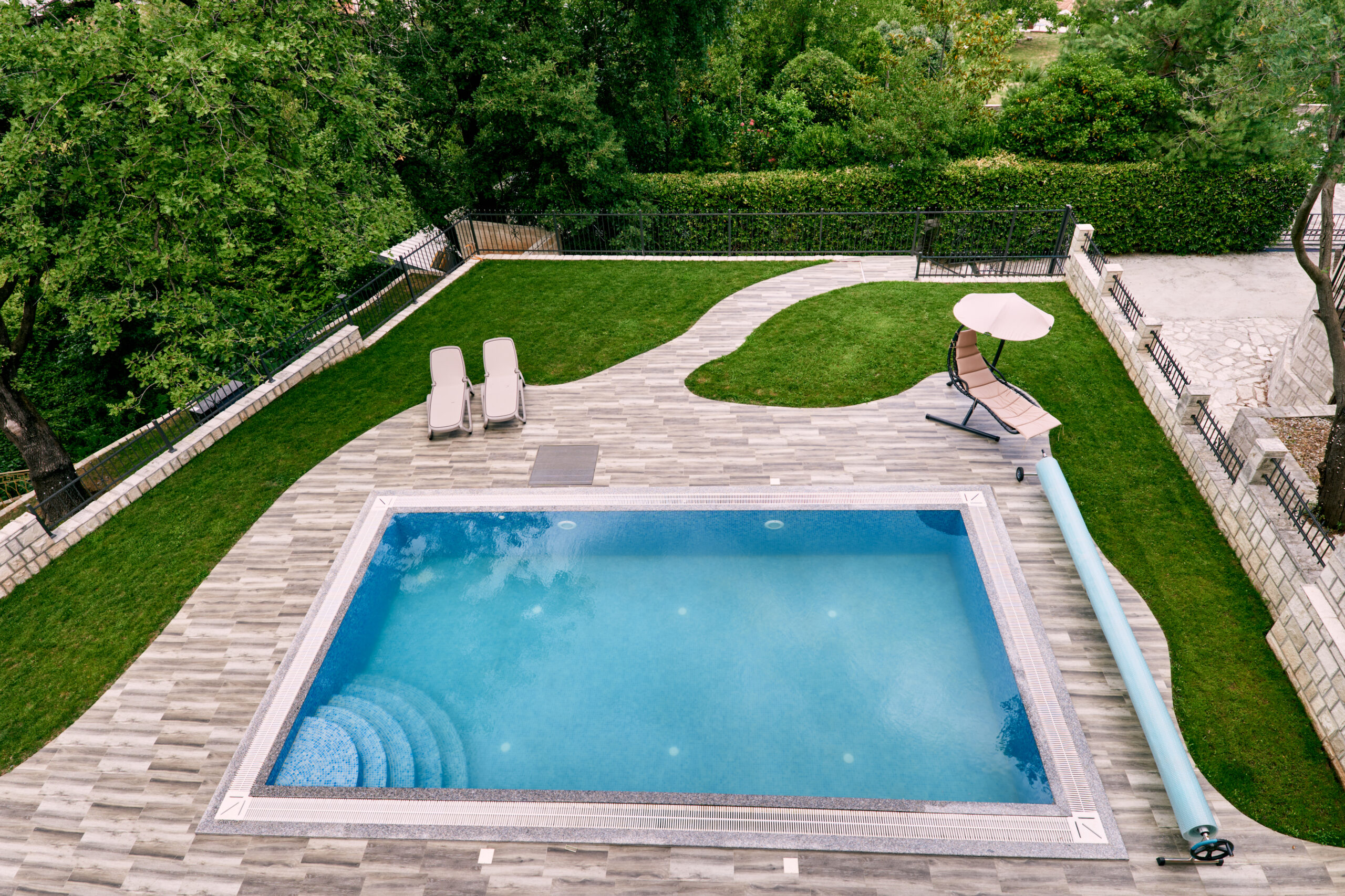 Sun loungers stand on a green lawn near a rectangular pool in the yard. Top view. High quality photo