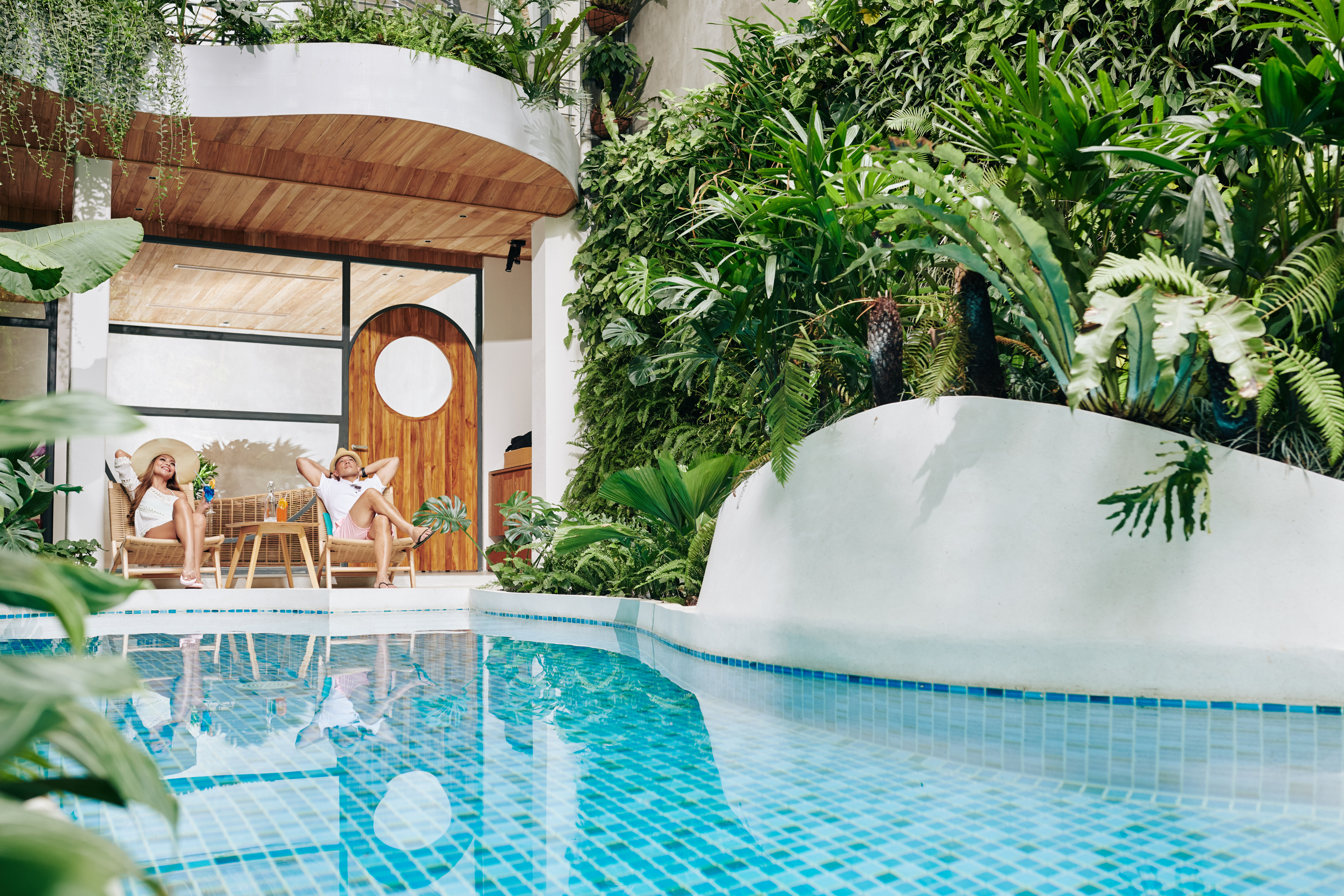 Happy couple daydreaming in chaise-lounges by swimming pool of spa hotel and drinking fruit cocktails