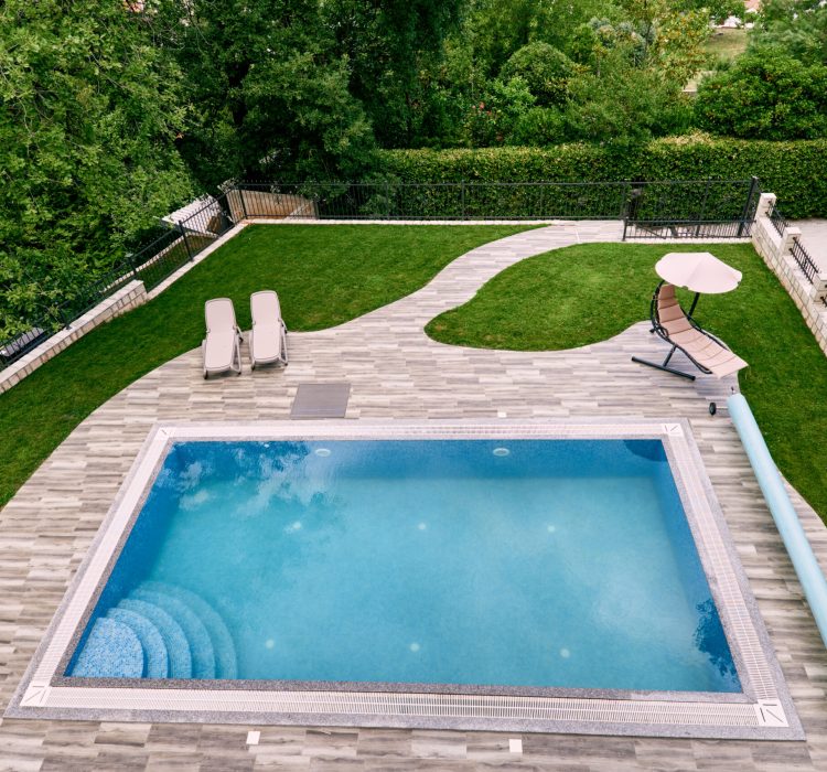 Sun loungers stand on a green lawn near a rectangular pool in the yard. Top view. High quality photo